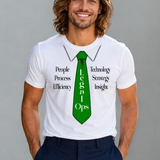 A smiling man with long brown hair stands against a plain gray background wearing a white graphic T-shirt with a green tie design and dark navy pants.